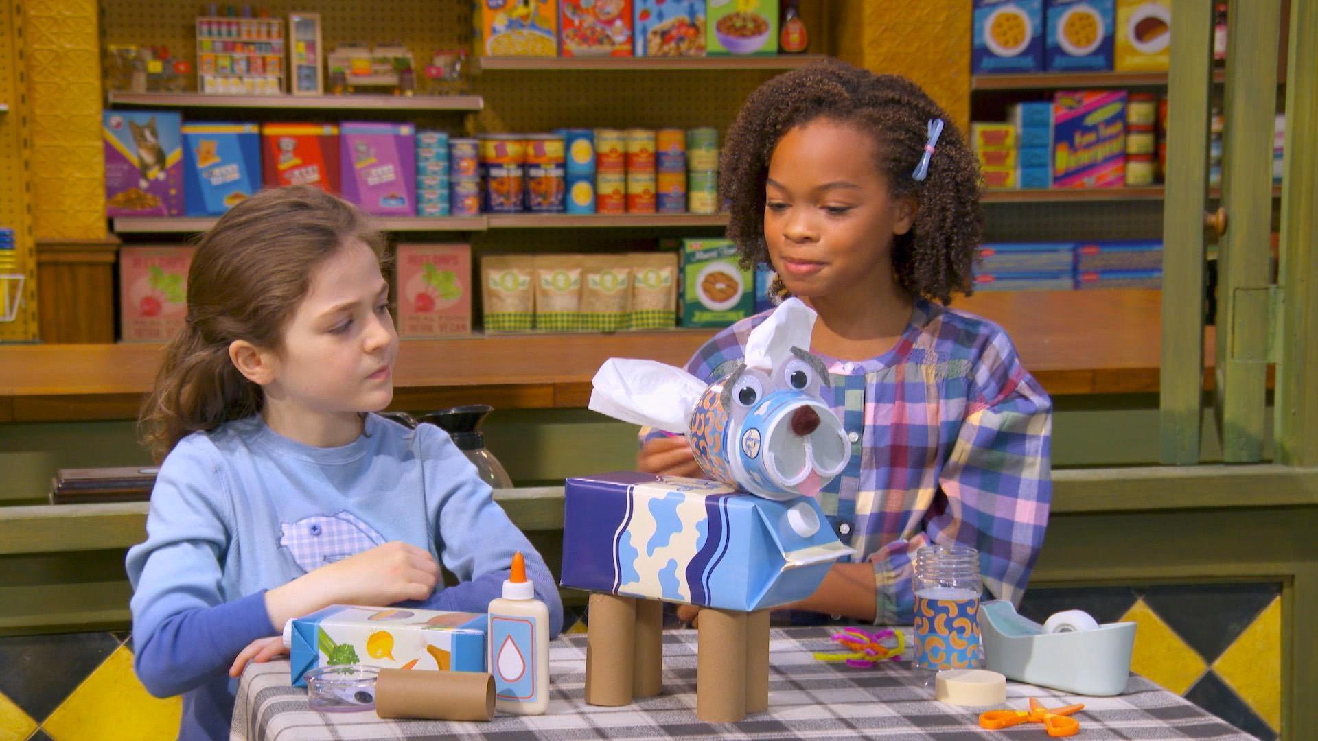Two girls are building a robot dog and are trying to figure out what to use for his tail.